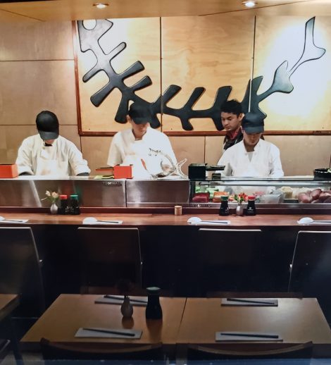 5 sushi chefs standing behind yoshimasa sushi display cases in a restaurant